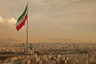 Iran flag waving in the wind above skyline of Tehran lit by orange glow of sunset.