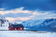 Rød hytte ved sjøen i snødekt landskap.