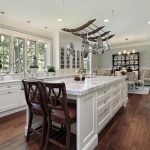 A bright kitchen with white marble countertops and wooden chairs.