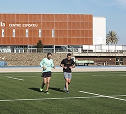 Dues persones corren en una pista exterior d'un centre esportiu municipal 