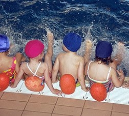 Nens i nenes asseguts a la vora de la piscina donant puntades de peu a l'aigua