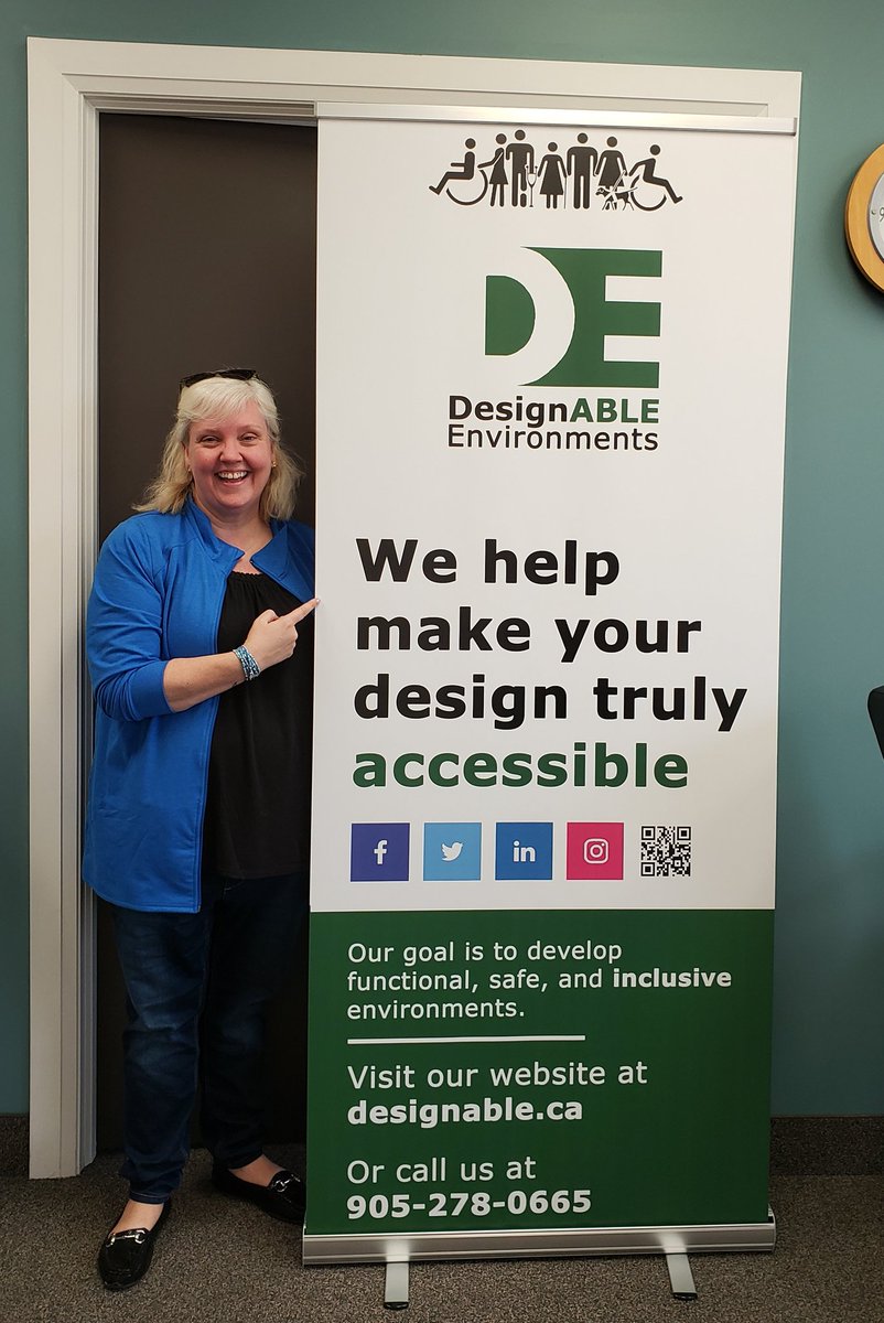 our Thea Kurdi standing next to our conference banner with our slogan "We help make your design truly accessible"