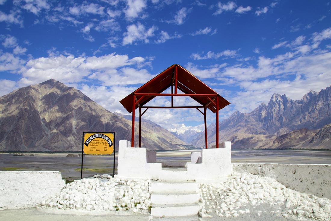 Masherbrum viewpoint with a red roof sheltering would-be visitors as they are afforded a brilliant view of vast waters surrounded by majestic mountains.