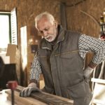 Mature carpenter experiencing back pain while checking wood plank in his workshop