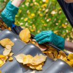 Man with gloved hands cleaning out leaves from a gutter