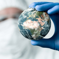 Person wearing protective equipment covering most of body and face, with a gloved hand holding up a globe