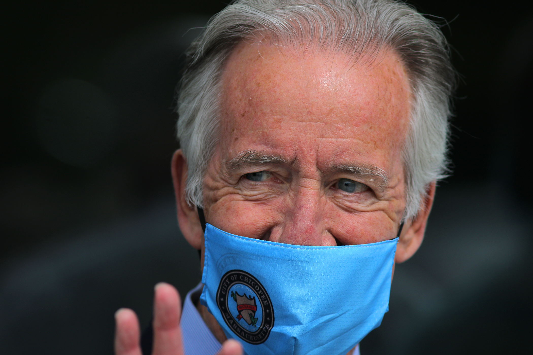 Richard Neal wearing a mask and smiling and waving to a camera.