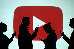 Silhouettes of mobile users are seen next to a screen projection of Youtube logo in this picture illustration taken March 28, 2018.  REUTERS/Dado Ruvic/Illustration