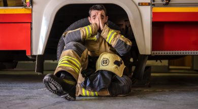 Picture of tired fireman sitting on floor near red fire truck