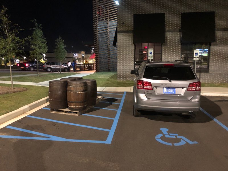 An accessible parking space with an access aisle on the left side. A shipping palette with four whiskey barrels on it sits in the middle of the access aisle.