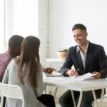 Friendly smiling architect or real estate agent consulting interracial couple