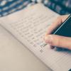 Closeup photo of a person's hand holding a pen and writing a checklist in a notebook 