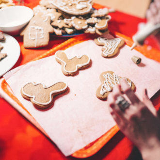 Several hands are decorating gingerbread cookies at a table.