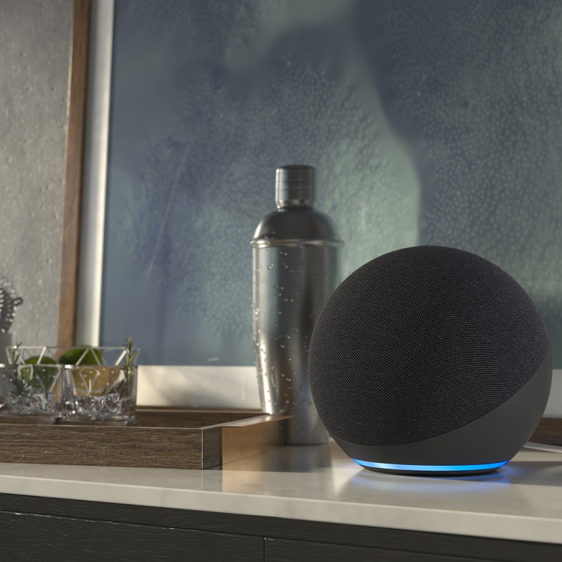 An image of an Echo device sitting on a side table next to a framed artwork and other home decor.