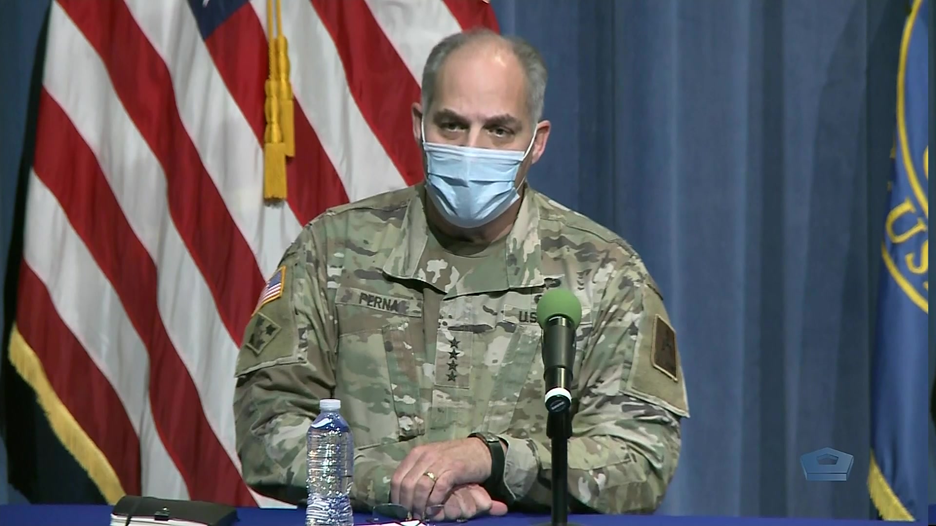 A soldier sits a table in front of a microphone. 