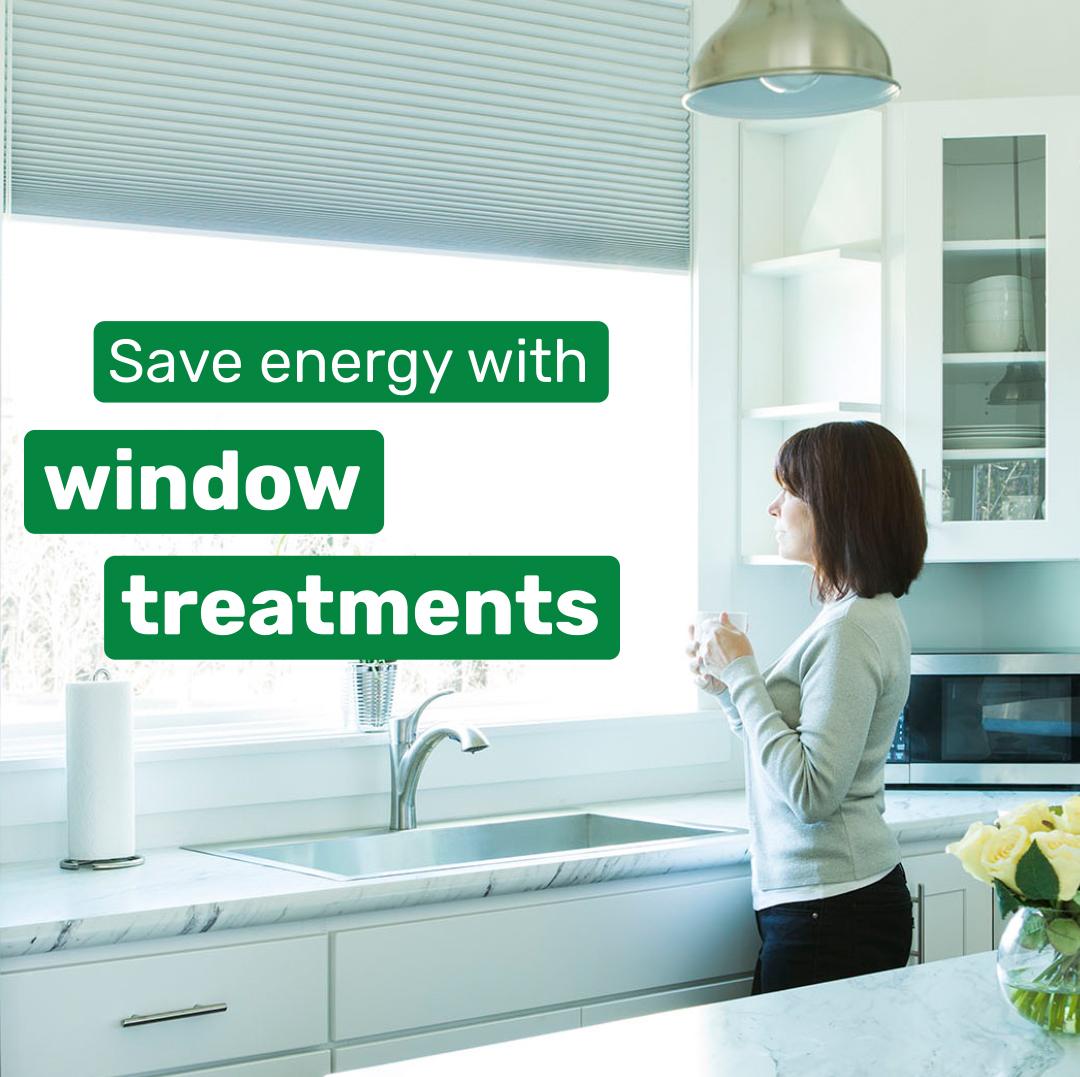 Womand stands in kitchen looking out her windows with energy-efficient window treatments.
