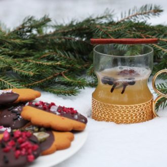 A plate of gingerbread cookies, a spruce branch and a drink cup are placed on a layer of snow.