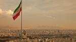 Iran flag waving in the wind above the skyline of Tehran lit by the orange glow of sunset.