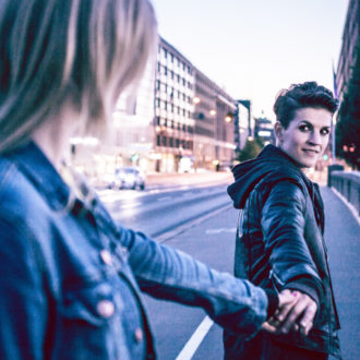 Two women holding hands on a street; the woman ahead has turned to look at the woman behind.