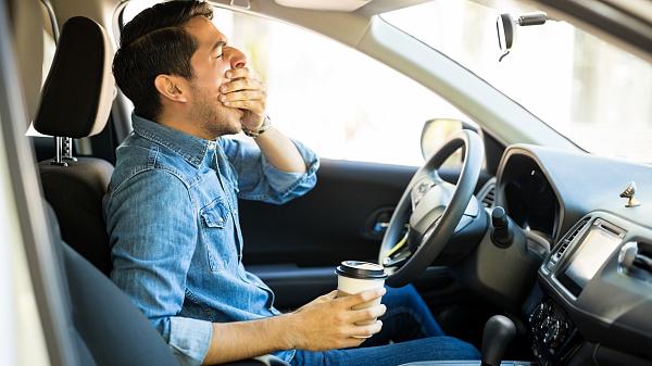 Tired man in a car, yawning and drinking take away coffee.