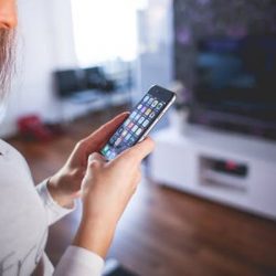 A woman in a grey shirt turns on the television with her smart phone.