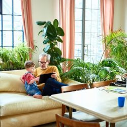 Grandfather and grandson on couch surrounded by live palms, ficus, and ferns.