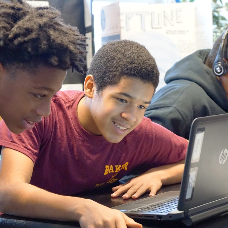 Students use a laptop in a classroom while working together on a coding project.