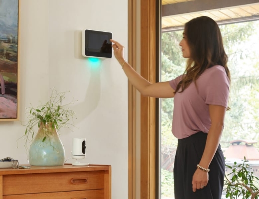 Woman touching the Vivint Smart Hub on white wall and view of the Vivint Indoor Camera on dresser