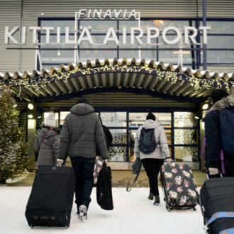 People pulling their suitcases towards a building with a sign that says Kittilä Airport.