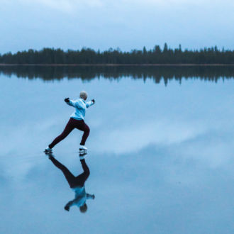 A woman ice skates across a lake whose surface reflects the sky.