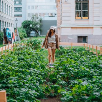 A woman stands in the middle of an urban garden plot.