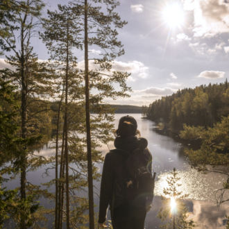 A hiker takes in a sunlit view of lake and forest in Repovesi National Park, southern Finland.