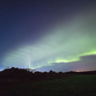 Green aurora borealis in a night sky over a field.