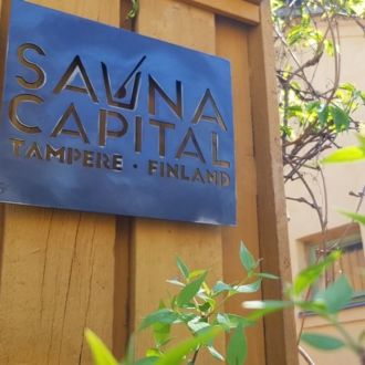 A blue sign on a yellow wooden wall reads, Sauna Capital, Tampere, Finland.