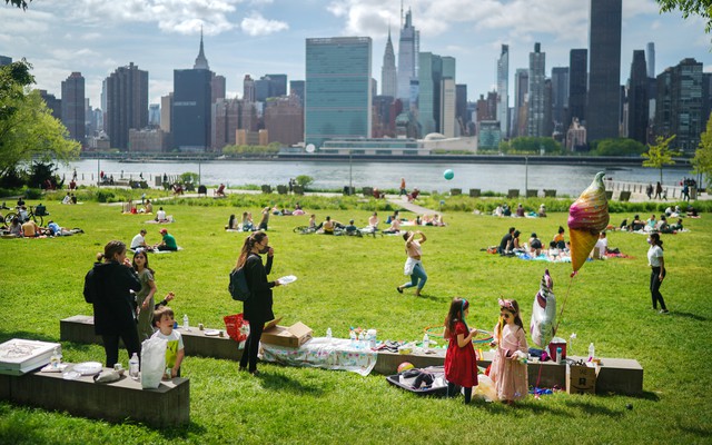 A birthday party in a park on a sunny day, with people relaxing in the background an urban skyline in the distance