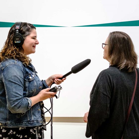 podcast host holding microphone towards Museum visitor in front or Herrera painting