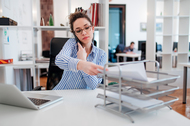 A woman handling a computer, smartphone, and files.