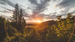 Sun setting in the background with cloudy sky and trees in the foreground.