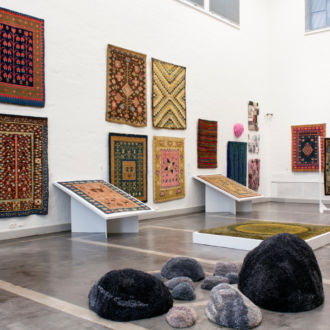 In a spacious museum gallery, rugs and tapestries are hanging on the walls.