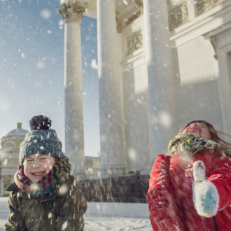 Two children are throwing snow into the air in front of the buildings of downtown Helsinki.