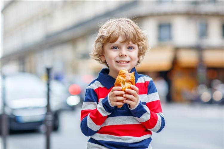 Happy child on street eating a croissant.