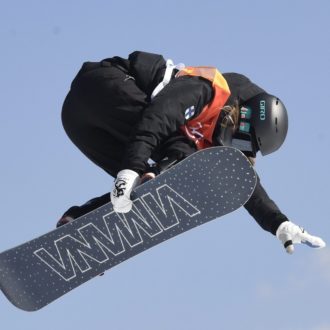 Uma mulher em uma prancha de snowboard está no ar, o céu visível atrás dela.