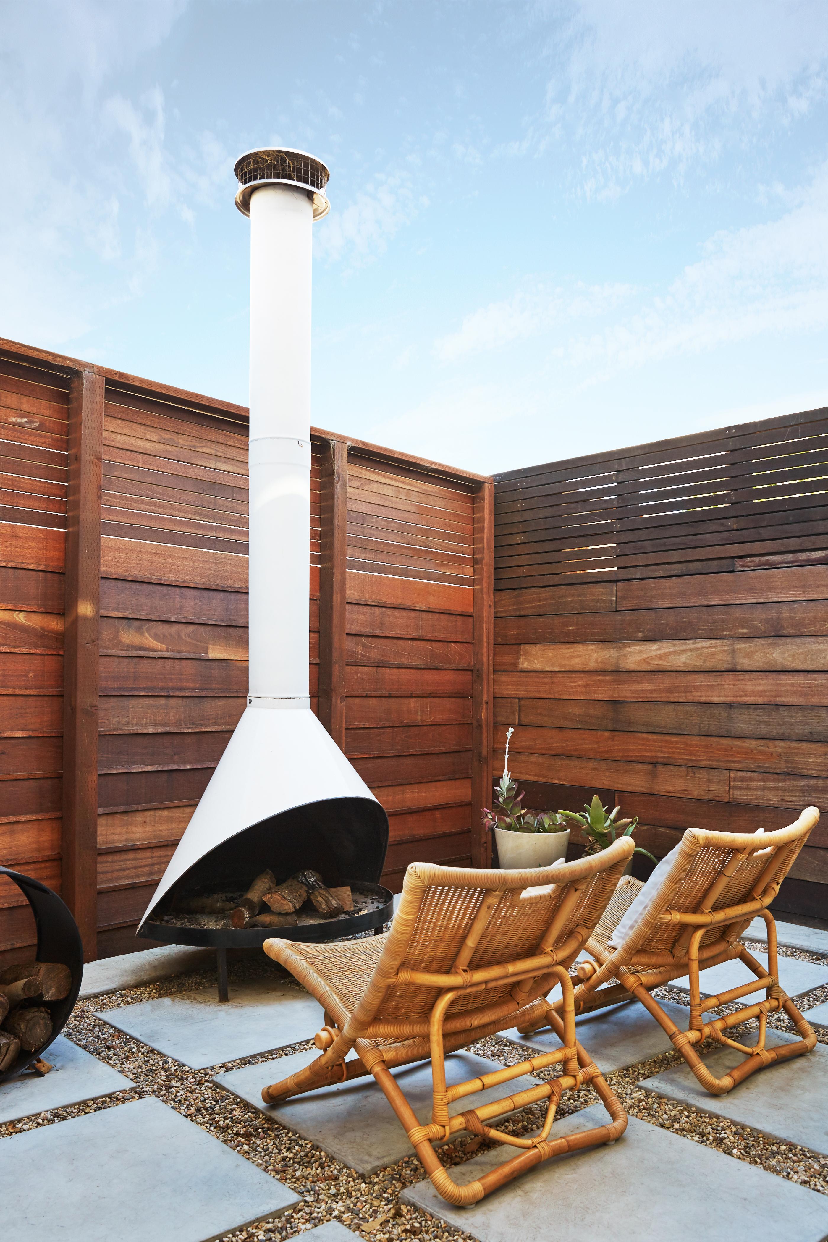 A high wooden fence provides privacy for the small outdoor patio, equipped with two woven chairs and an outdoor fireplace.