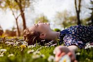 A young girl laying in the grass in the spring sun surrounded by daisies.