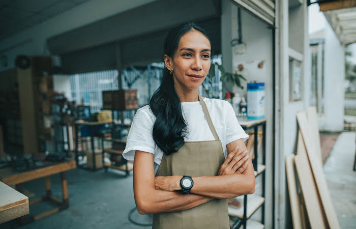 Woman standing in a studio wearing a canvas apron with her arms folded