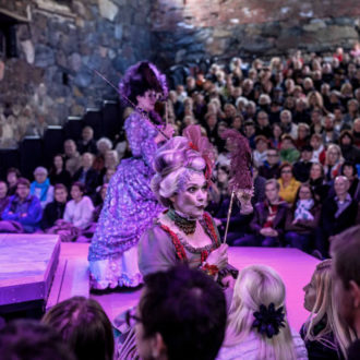 Two women in rococo-styled outfits performing on a stage with a large crowd watching.