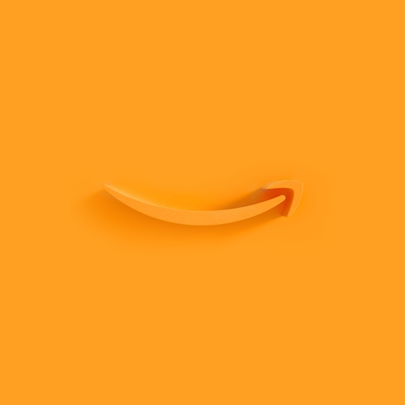 Amazon's orange smile logo appears as an extruded plastic form on an orange background, with a shadow cast by a light source from the right