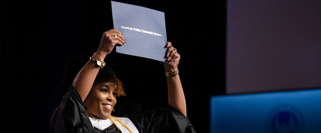 Female alumna holding diploma on Commencement stage.