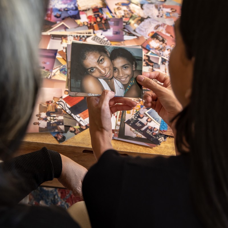 Two figures seen from behind look at a photo of a woman and a girl.