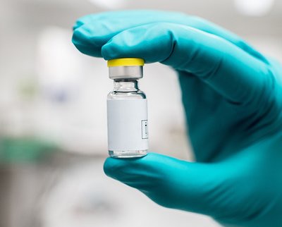 a hand wearing blue glove holding a vaccine vial.